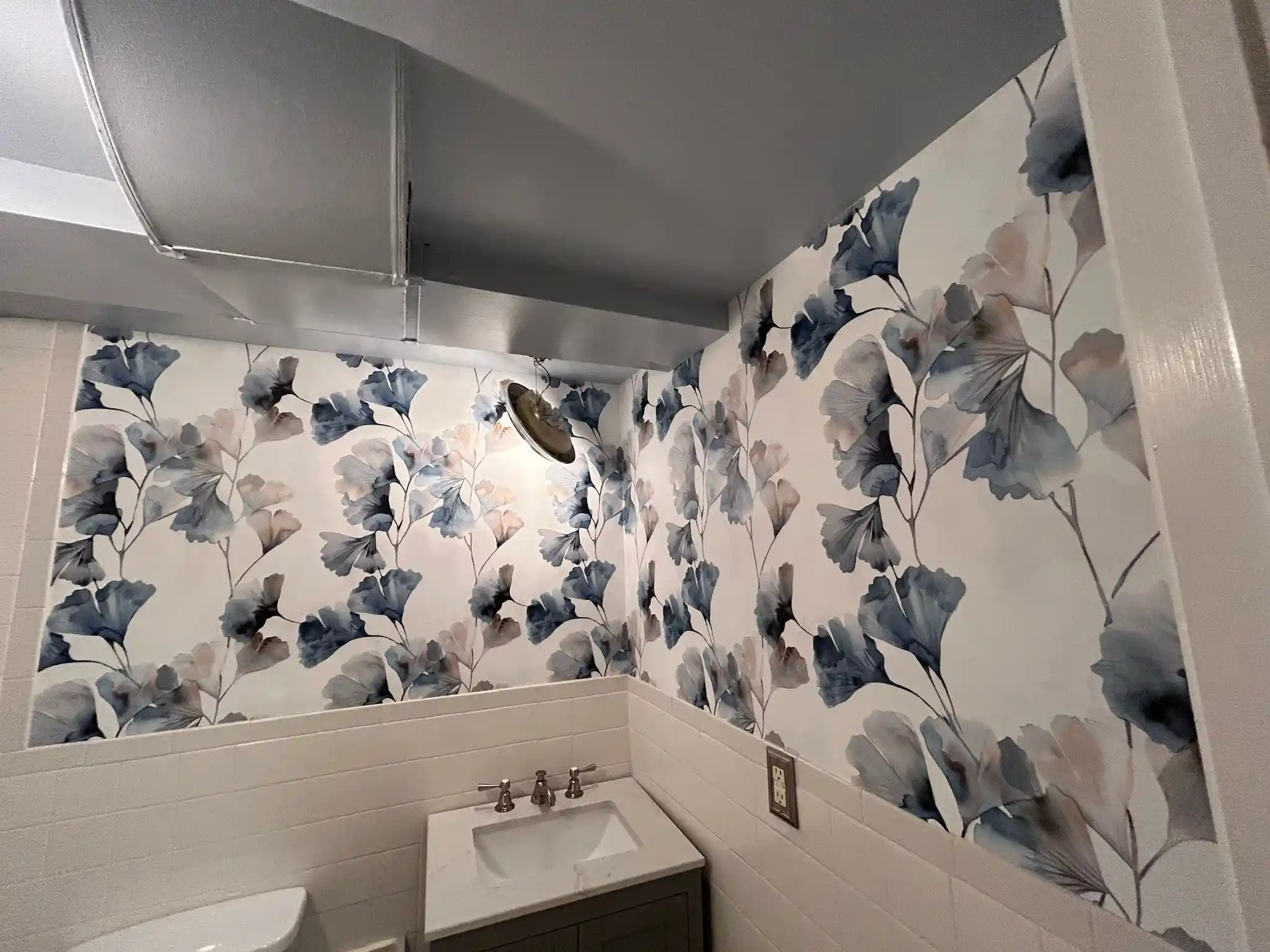 Blue and gray floral wallpaper wrapping a small bathroom wall