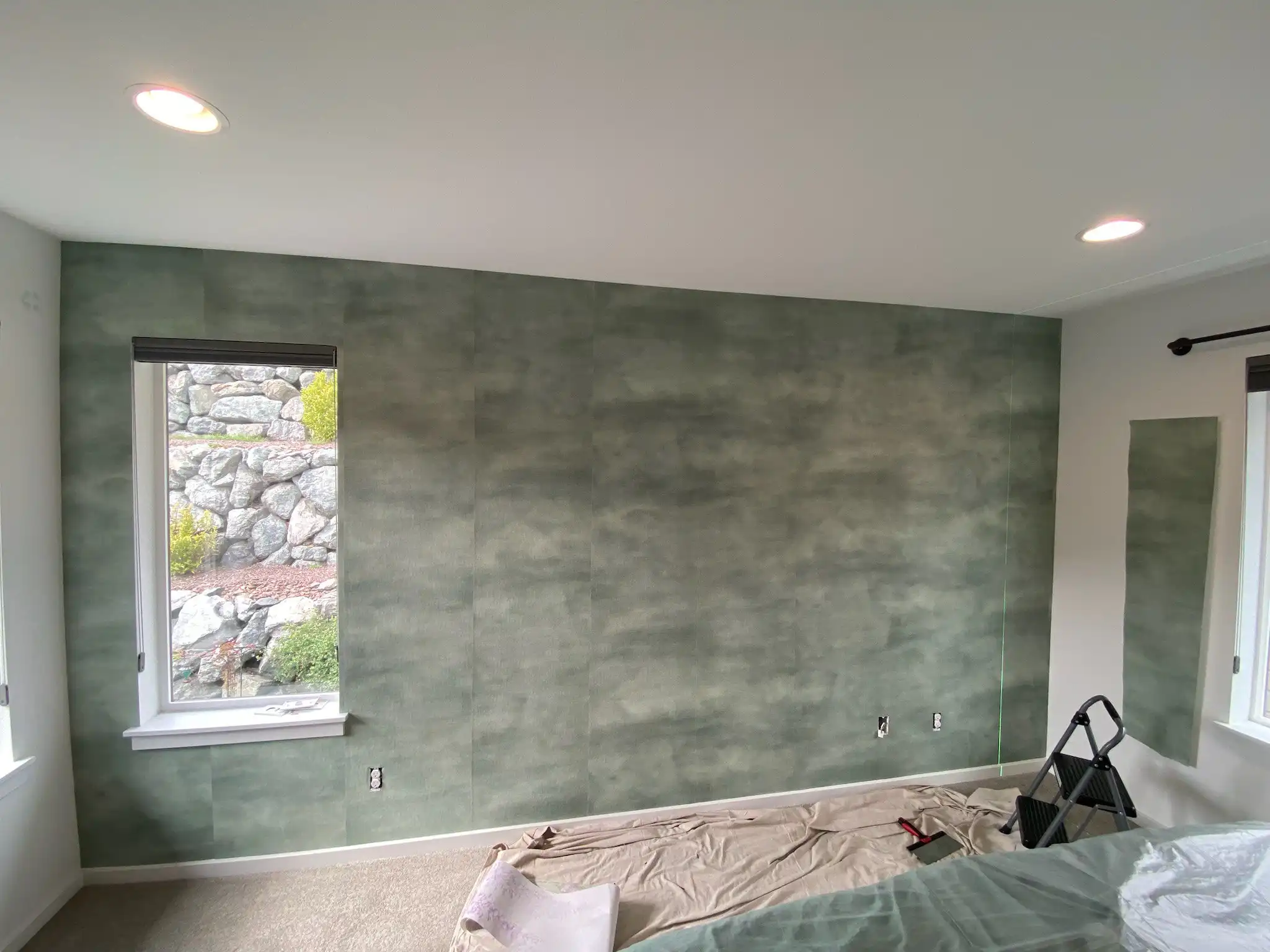 Soft green textured wallcovering on a prepared feature wall beside a window